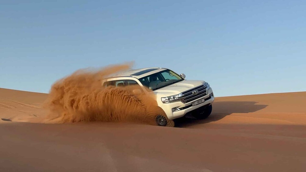 A white SUV driving through a desert with sand being kicked up by its tires. 1