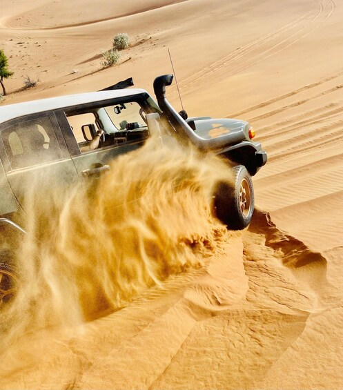 A vehicle driving through a desert with sand being kicked up by its tires. 4