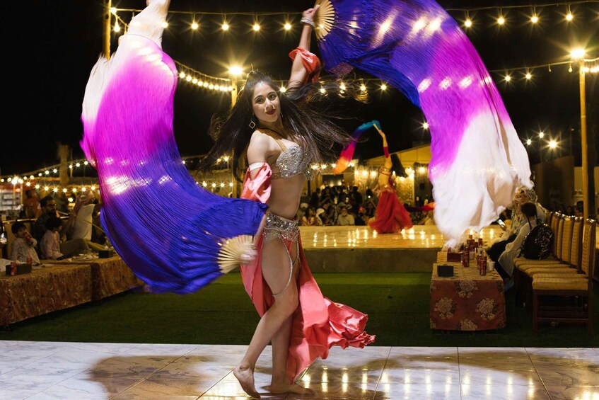 A performer with a flowing purple and white costume, performing on a stage with an audience in the background. 3