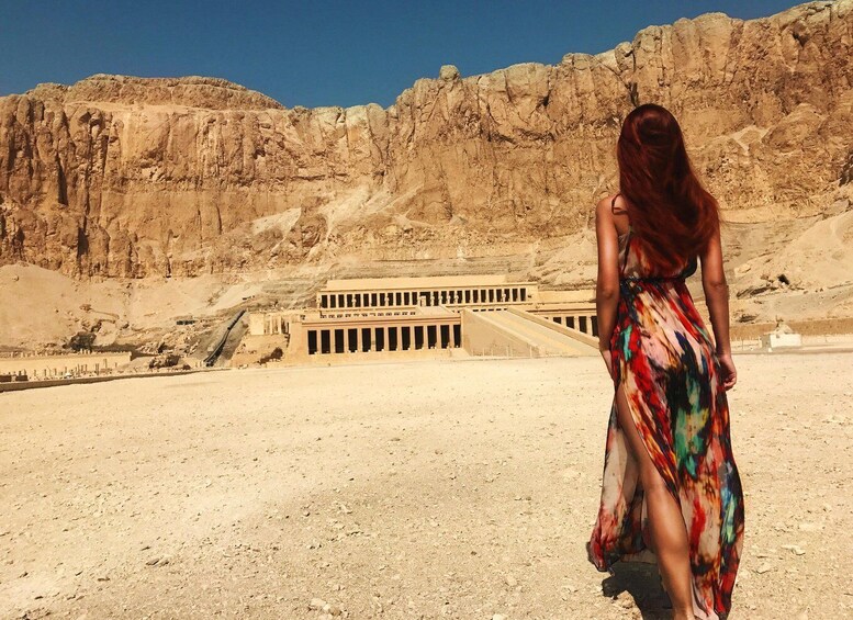 A person in a colorful dress standing in a desert with a large ancient Egyptian temple in the background. 2