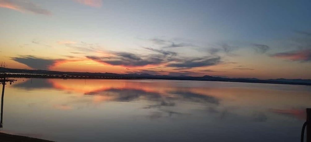 A calm lake with a sunset, a pier, and distant mountains. 4