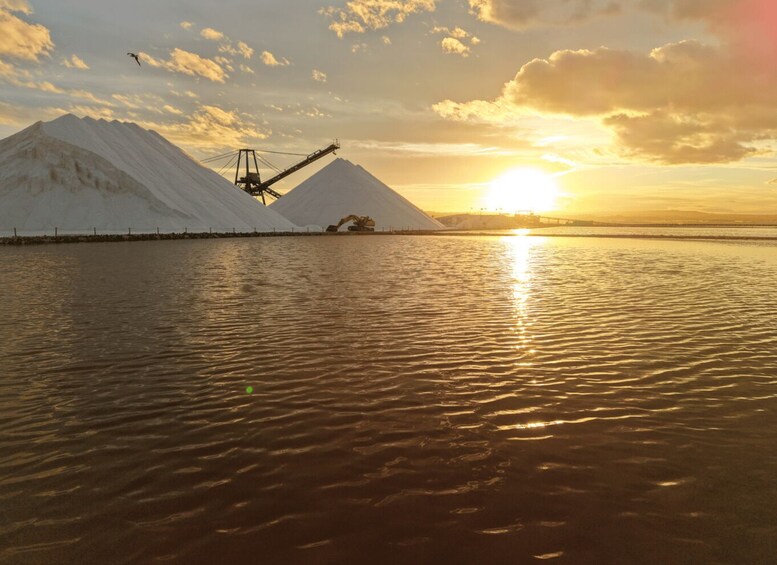 A sunset over a body of water with a large snow-covered mountain and a mining operation in the background. 5