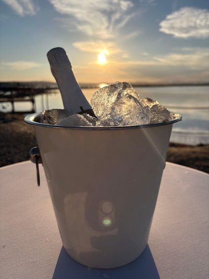 A metal bucket filled with ice cubes on a table with a sunset in the background. 3