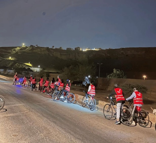 A group of cyclists in red vests on a road at night. 1