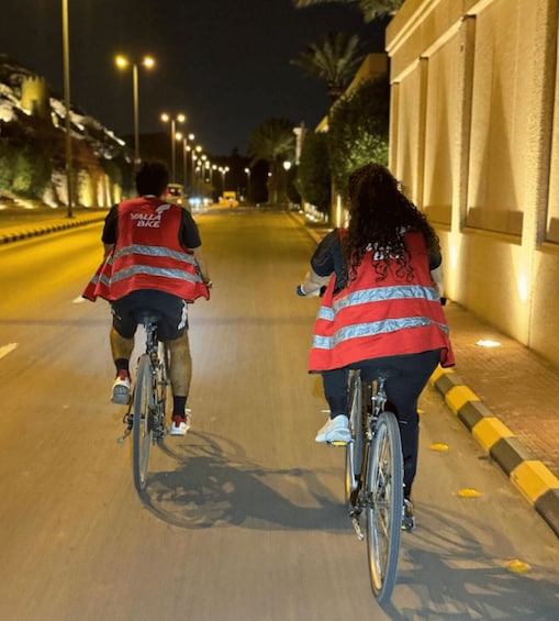 Two cyclists on a city street at night, wearing reflective vests. 2