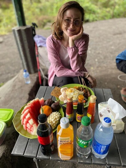 A person sitting at a picnic table with a meal, drinks, and condiments. 2