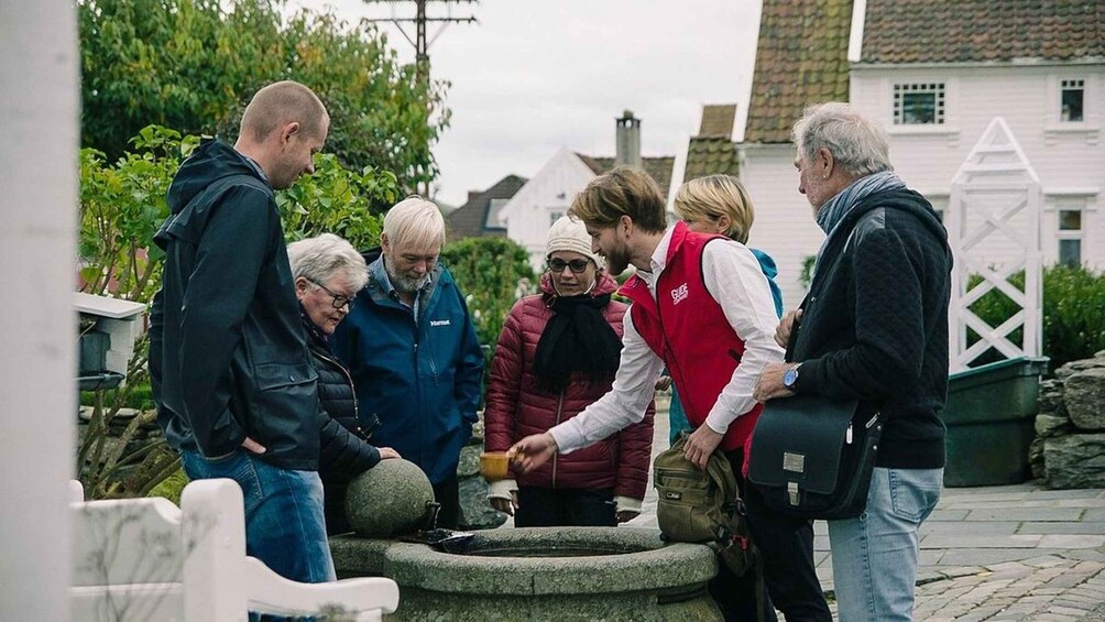 A group of people gathered around a stone fountain in a residential area with houses and greenery in the background. 1