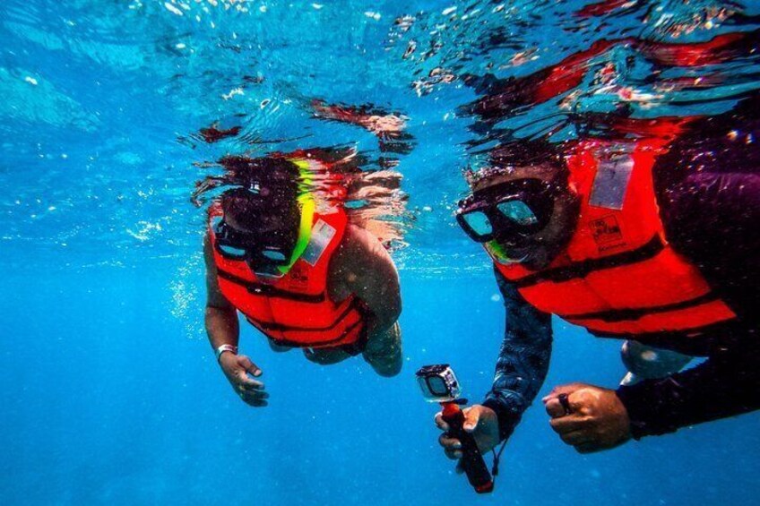 Two people underwater in a pool, wearing red life jackets and goggles. 4