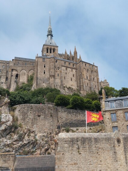 A historic castle with a prominent spire, a flag, and a stone wall. 4