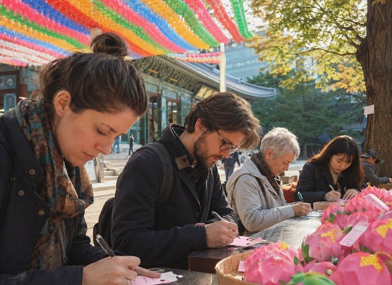 People writing at a table with pink flowers and a colorful canopy overhead. 2