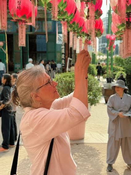 A person reaching up to a string of red lanterns with hanging tags. 5
