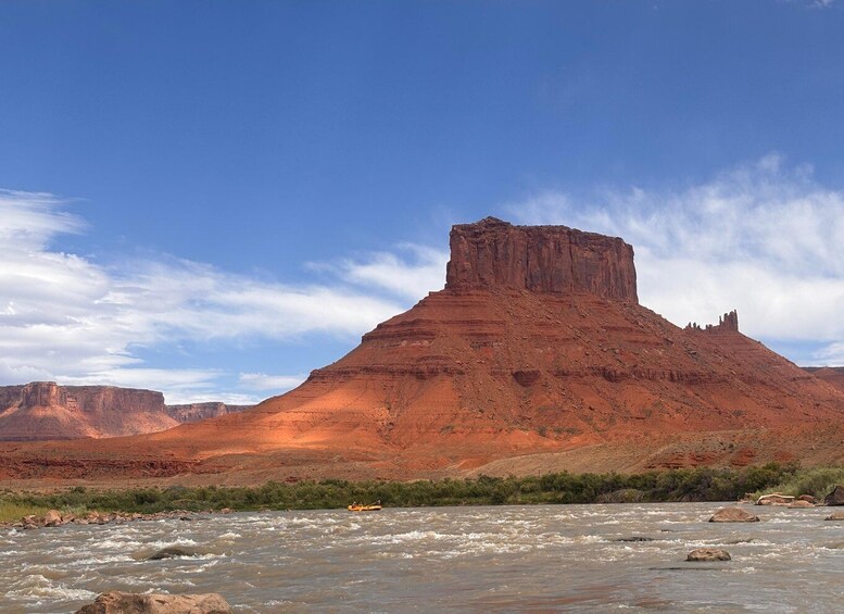 A river with a raft, a prominent red rock formation, and a clear blue sky. 3