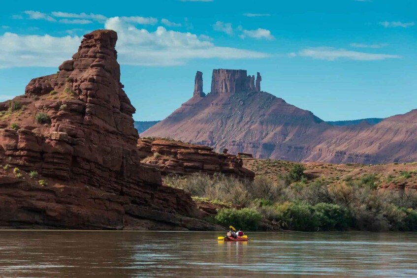 A kayaker on a river with red rock formations and a mesa in the background. 5