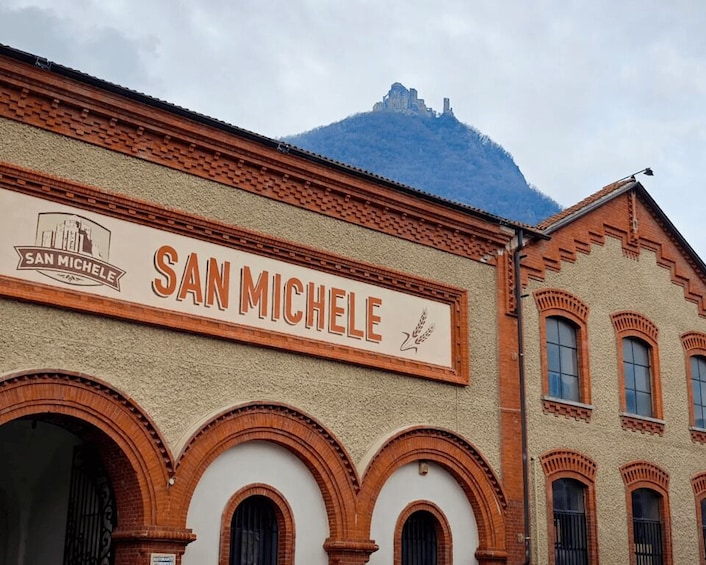 A building with a sign reading 'SAN MICHELE' and a mountain in the background. 2