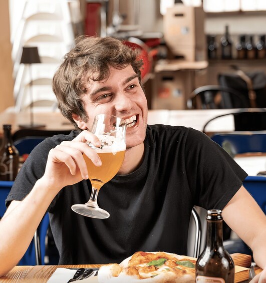 A person sitting at a table with a glass of beer and a pizza. 1