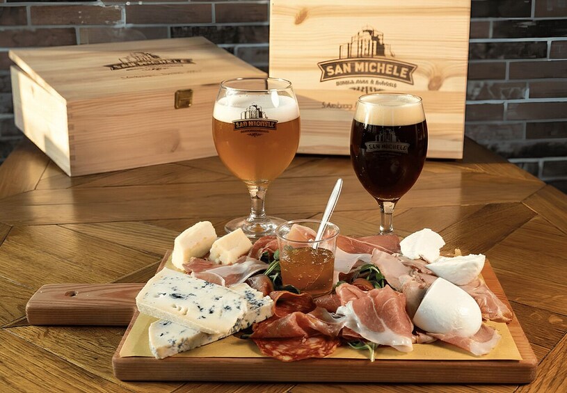 A wooden board with cheese, meats, and drinks, and a San Michele branded box in the background. 5