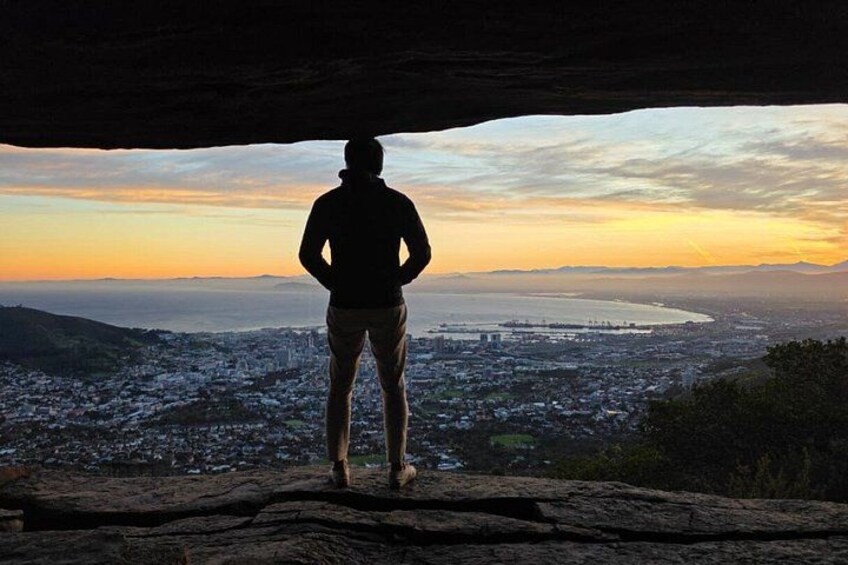 A person standing on a rock with a cityscape and sunset in the background. 1