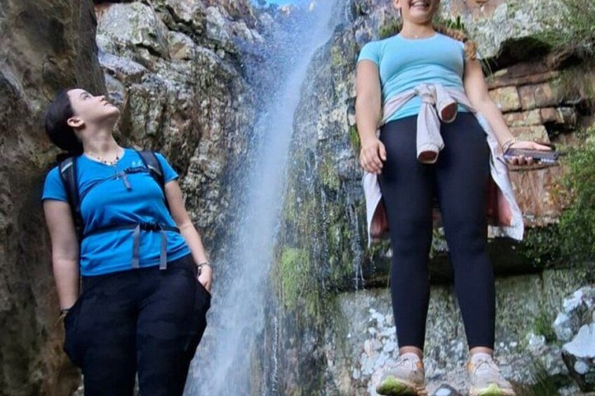 Two people standing near a waterfall with rocky terrain. 2
