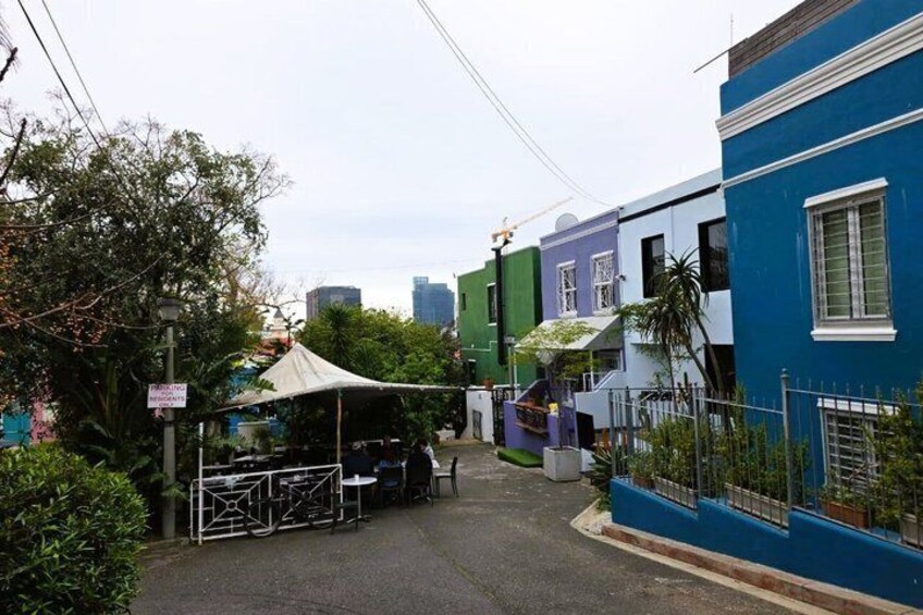 A narrow street with colorful houses, a white tent, and a parked car. 3