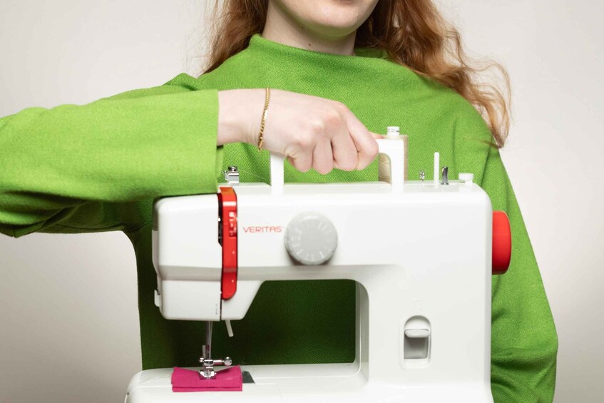A person using a white sewing machine with a red knob and a green fabric. 2