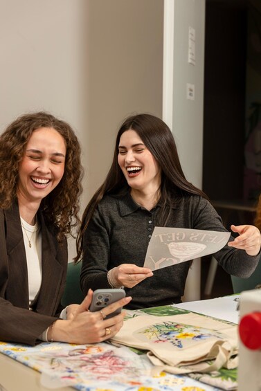 Two people at a table with a floral tablecloth, one holding a phone and the other holding a paper. 1