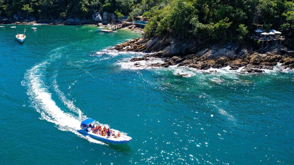 A boat with passengers navigating a turquoise coastal waterway, surrounded by rocky cliffs and lush greenery. 2