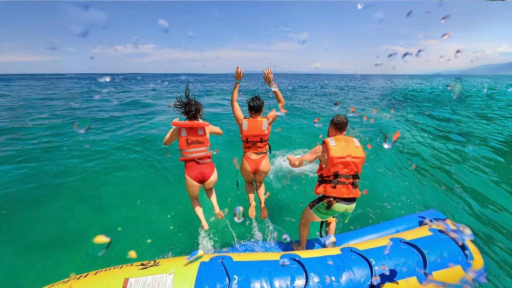 Three people jumping off a raft into turquoise ocean water. 4
