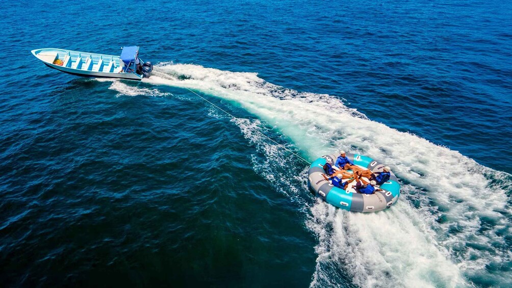 A speedboat towing a raft with people on a clear day over the ocean. 1