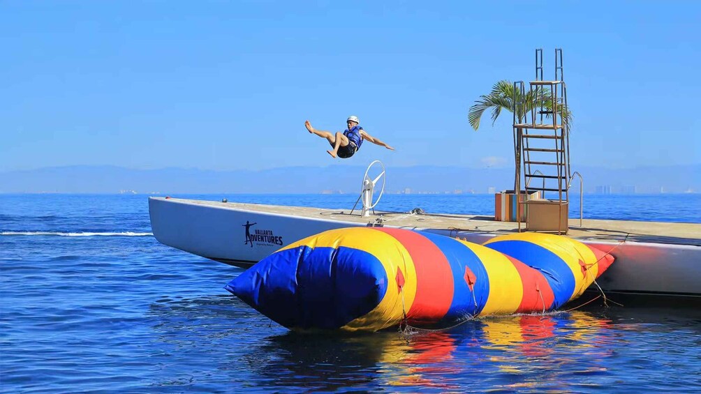 A person performing a backflip on a trampoline on a boat, with a clear blue sky and calm sea in the background. 3