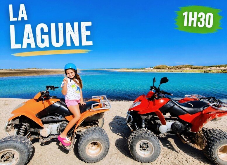 A child on an orange ATV and another on a red ATV by a clear blue lake. 2