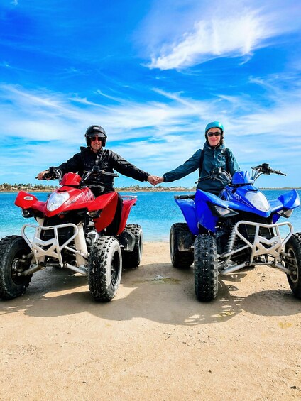 Two people on ATVs by a beach with a clear sky. 4