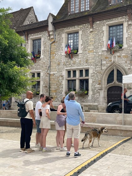A stone building with flags, people standing in front, and a dog on a leash. 4