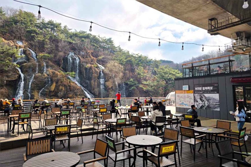 An outdoor café with tables and chairs, overlooking a waterfall and forested hillside. 5