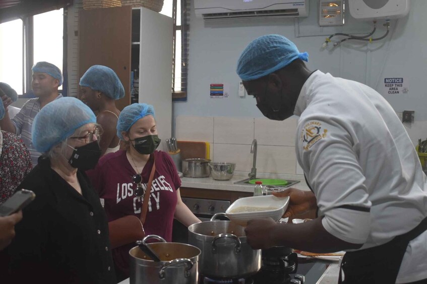 A group of people in a kitchen, some wearing hairnets and aprons, engaged in food preparation. 1
