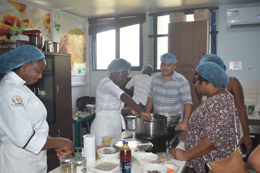 A kitchen with people preparing food, cooking pots, and various food containers. 3
