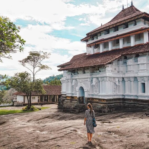 A white temple with a tiled roof, a woman in a dress, and a rocky landscape. 1