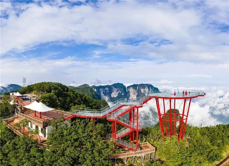 A glass walkway with red supports, overlooking a mountainous landscape. 1