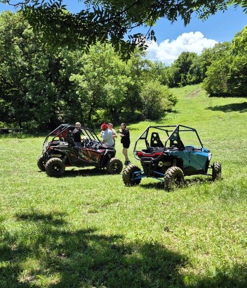 Two off-road vehicles in a grassy field with people around them. 3