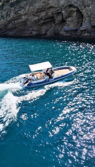 A speedboat with a canopy, moving through clear blue water with a rocky cliff in the background. 5