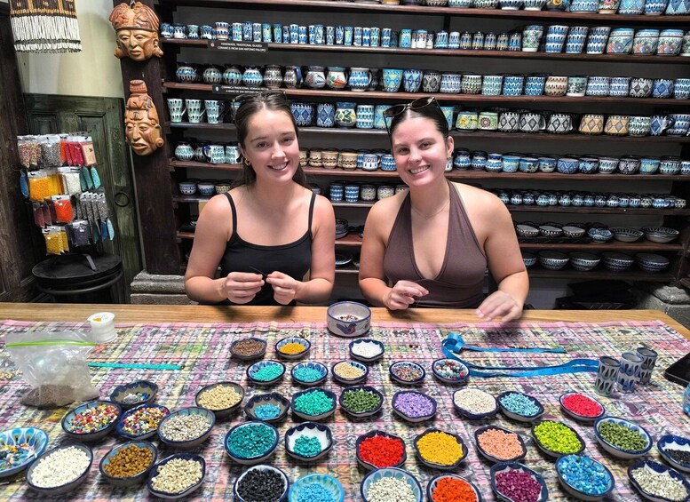 Two people seated at a table with various colorful beads and ceramic items in the background. 1