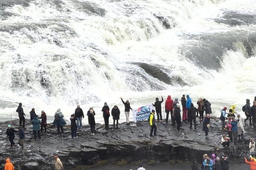 A group of people standing on a rocky shore watching a waterfall. 2
