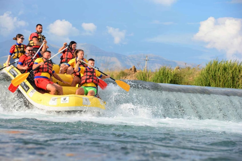 A group of people in a yellow raft navigating a water channel with a mountainous landscape in the background. 1
