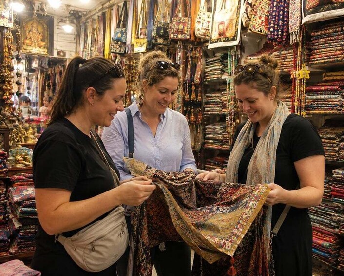 Three people examining a patterned fabric in a market filled with textiles. 3