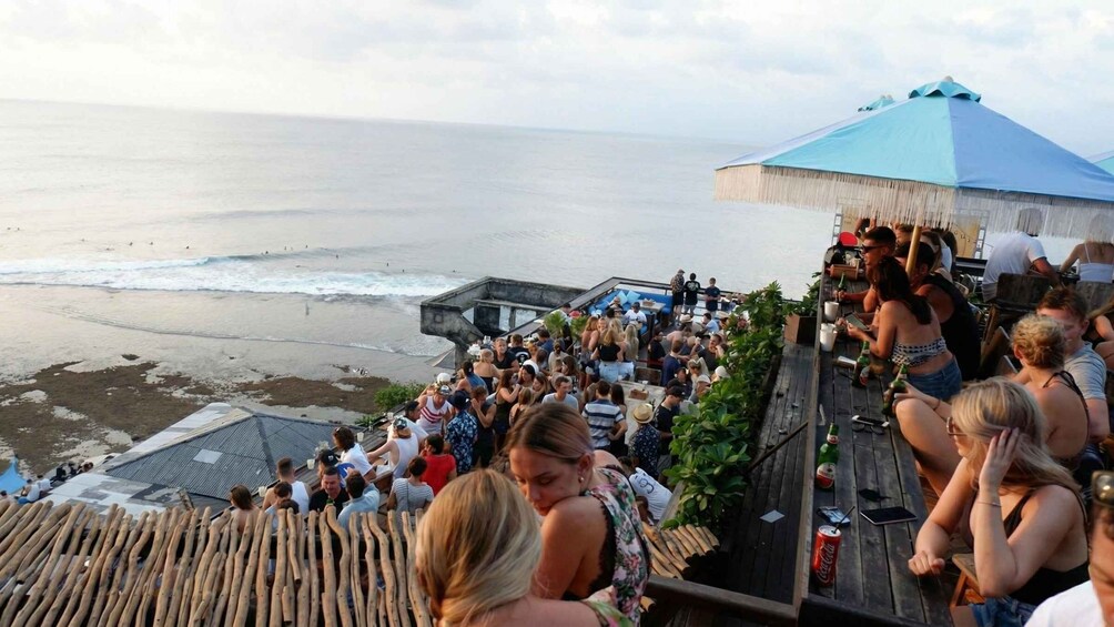 A crowded beachside event with a stage and a large tent. 1