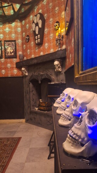 A room with a patterned wallpaper, a fireplace with skull decorations, and a table with illuminated skull models. 1
