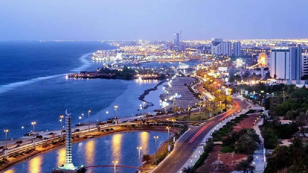 A coastal cityscape at dusk with illuminated streets, a waterfront promenade, and high-rise buildings. 2