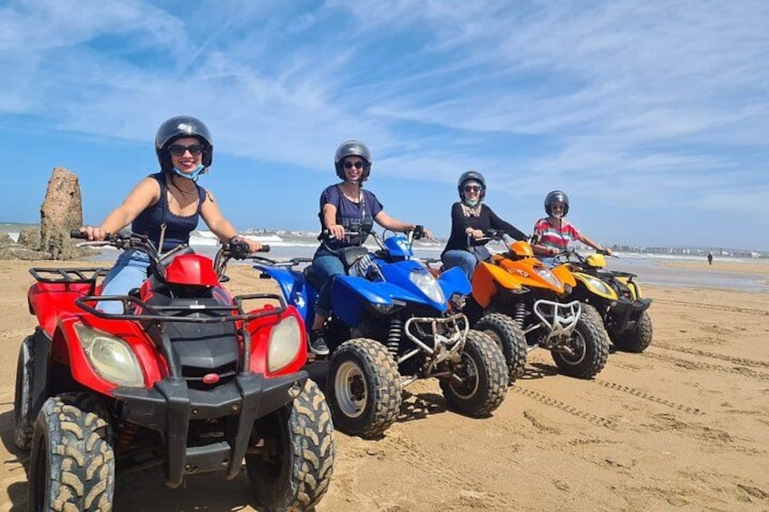 Three people riding ATVs on a sandy beach with a rocky formation in the background. 2