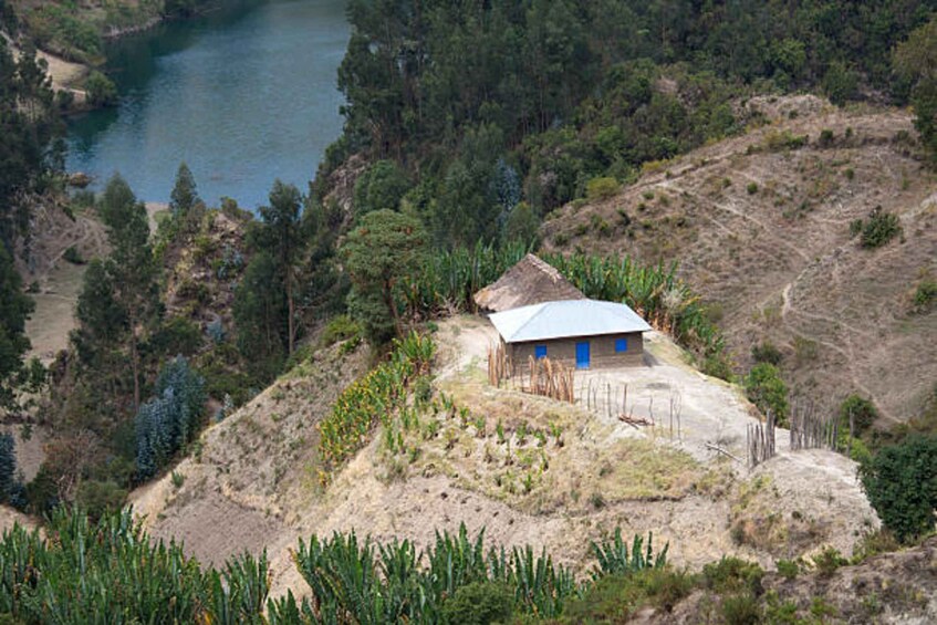 A small house with a blue roof surrounded by a dry, hilly landscape with sparse vegetation and a body of water in the background. 5