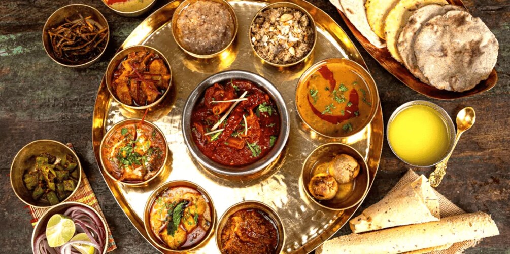 A variety of Indian dishes on a metal tray, including curries, bread, and a lemon wedge. 5