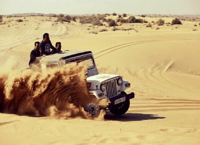 A white off-road vehicle driving through a desert with sand being kicked up by the tires. 4